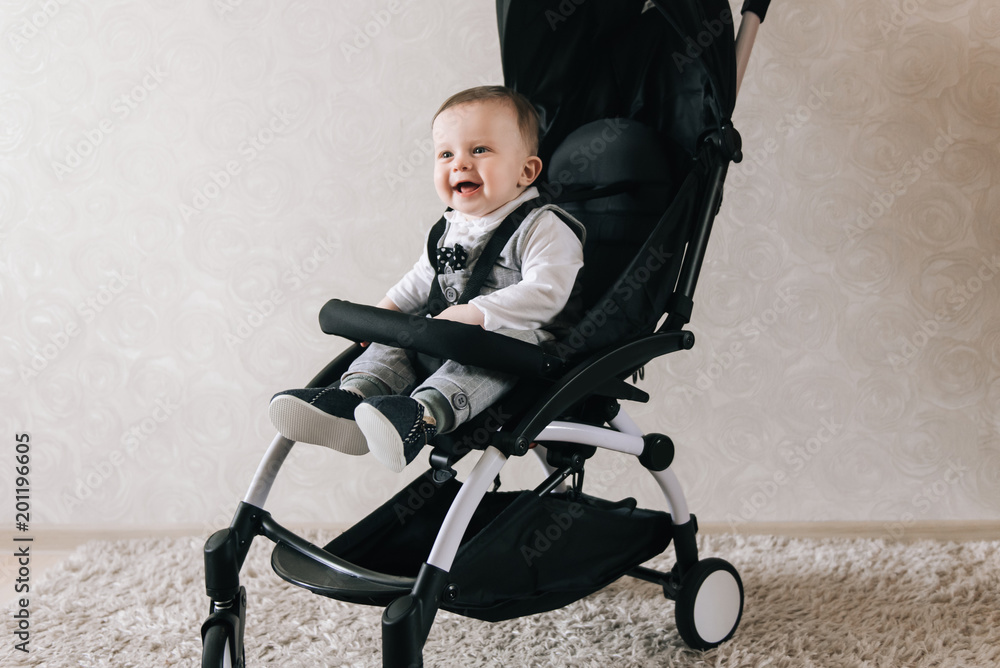 Little smiled boy sits in the baby buggy on the light background