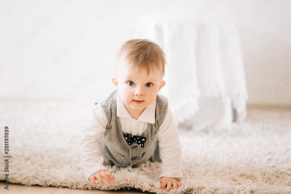 Fototapeta premium Cute happy kid in stylish gentleman suit crawling at home on light background