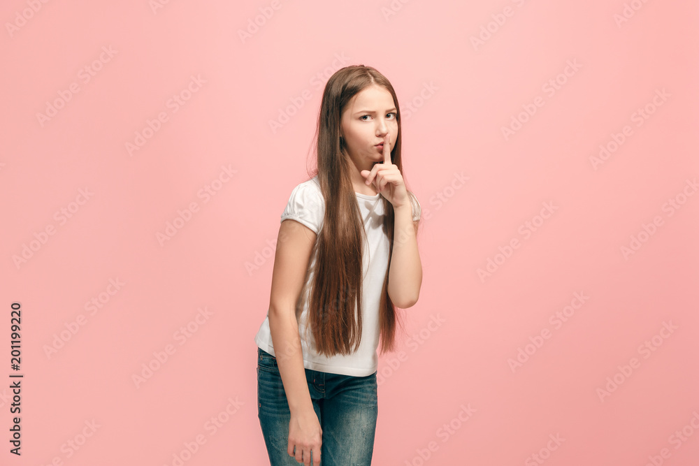 The young teen girl whispering a secret behind her hand over pink background The young teen girl whispering a secret behind her hand over pink background