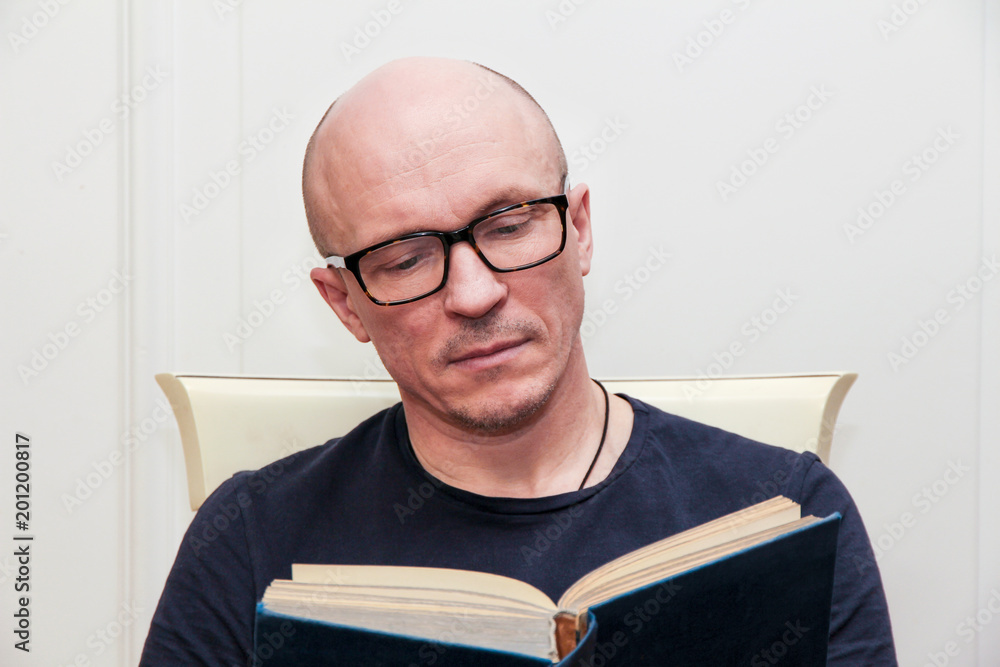 adult bald man in glasses reading a book adult bald man in glasses reading a book