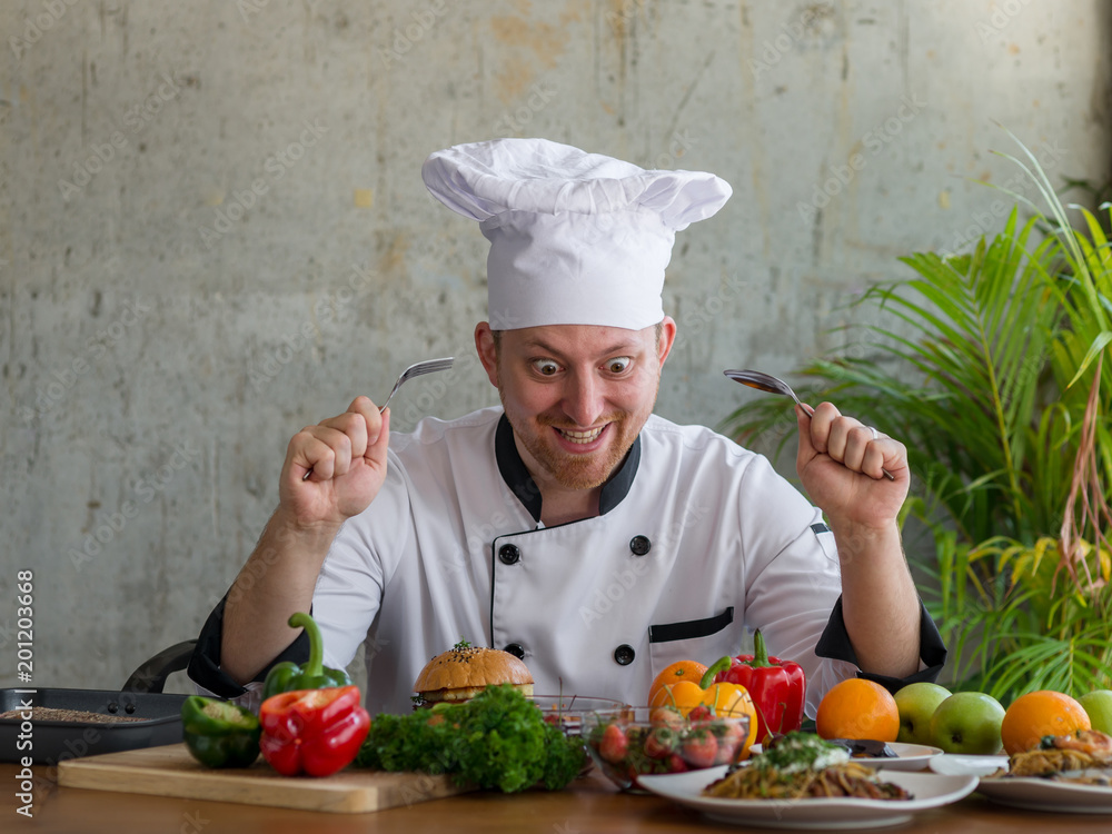 Crazy chef holding fork and spoon and looking at his food on table, work lifestyle concept. Crazy chef holding fork and spoon and looking at his food on table, work lifestyle concept.
