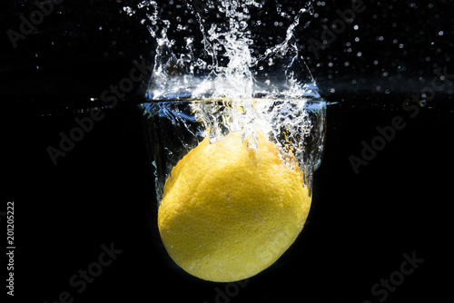 Lemon falling into the water and splashing drops on black background