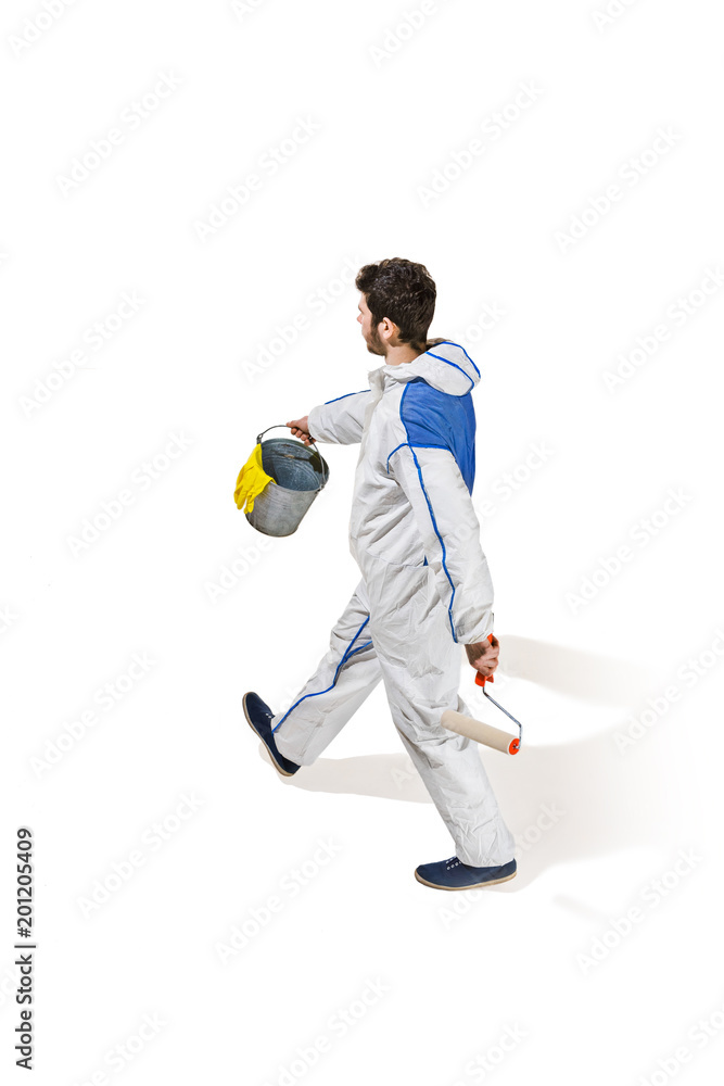 Fototapeta premium Young male decorator painting with a paint roller climbed a ladder isolated on white background.