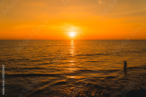 Beautiful beach sunset, silhouette  tourist walking along the ocean on sunset
