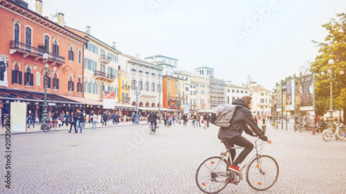Fototapeta Naklejka Na Ścianę i Meble -  Man riding a bike and crowd of people walking in the city square, blurred backgound.