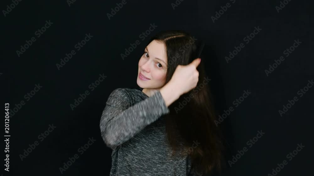 Smiling brunette woman looking at the camera and brushing her hair against a black background. Room for text. Smiling brunette woman looking at the camera and brushing her hair against a black background. Room for text.