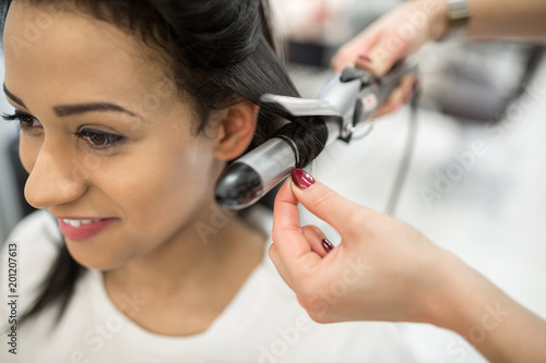 Happy young woman having hair stylized at hairdresser