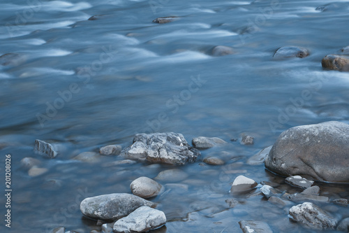Long exposure photo of a smooth water surface on small mountain river with rocks. Beautiful natural background.