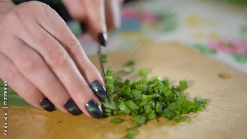 Woman chopping green onions on a wooden cutting board. Woman chopping green onions on a wooden cutting board.