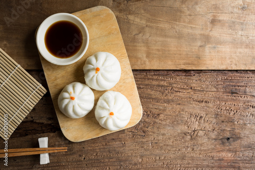 top view of steamed chinese bun (baozi) on cutting board served with soy sauce in rural kitchen, copy space for text. popular dim sum food menu.