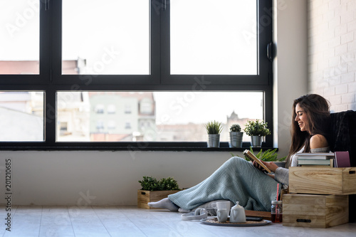 Beautiful young woman reading a book, enjoying by the window in modern apartment.  photo