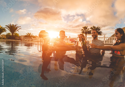 Happy friends cheering with champagne in pool party at sunset photo