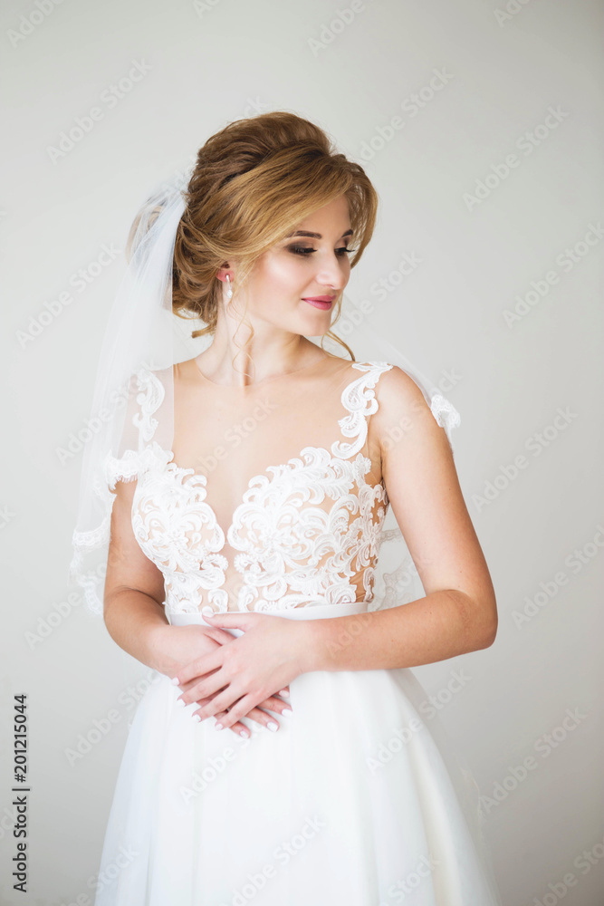Happy bride with beautiful smile in a beautiful white wedding dress in the background white wall. Beautiful lacy decollete Happy bride with beautiful smile in a beautiful white wedding dress in the background white wall. Beautiful lacy decollete