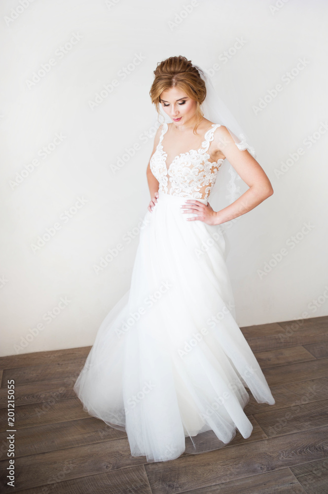 Happy bride with beautiful smile in a beautiful white wedding dress in the background white wall. Beautiful lacy decollete Happy bride with beautiful smile in a beautiful white wedding dress in the background white wall. Beautiful lacy decollete
