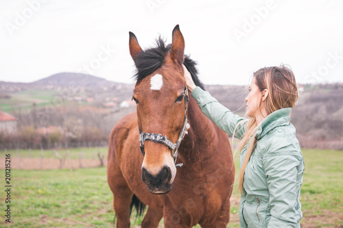 Beautiful young woman on the ranch bonding with a brown horse. 