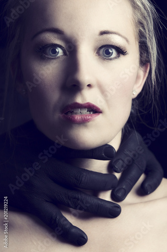 Fotografie Frightened blonde woman grabbed by black hands on her neck to strangle