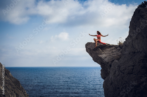 Woman on the cliff.At the bottom of the cliff is a deep, blue sea.The legs are delicately intertwined, the arms are apart. Beauty forms. Wildness. Freedom. Happiness. Implementation. Follow the dream.