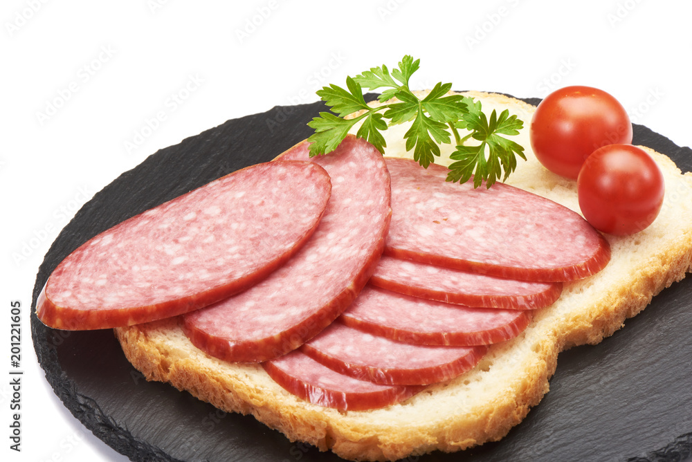 Tasty appetizer of thinly sliced spicy salami on wholewheat bread with a seed crust and liberal spread of butter or margarine topped with parsley, on a stone rustic board isolated on white background Tasty appetizer of thinly sliced spicy salami on wholewheat bread with a seed crust and liberal spread of butter or margarine topped with parsley, on a stone rustic board isolated on white background