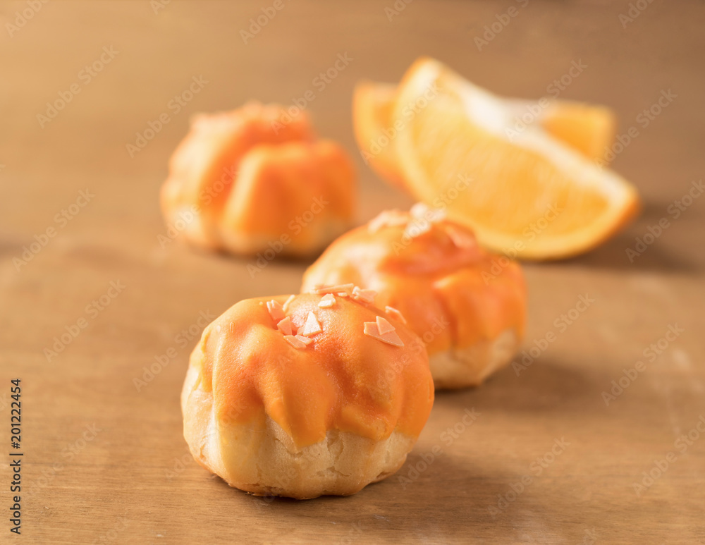 Fresh air Cake profiterole decorated with orange glaze on a wooden background. Selective focus. Fresh air Cake profiterole decorated with orange glaze on a wooden background. Selective focus.