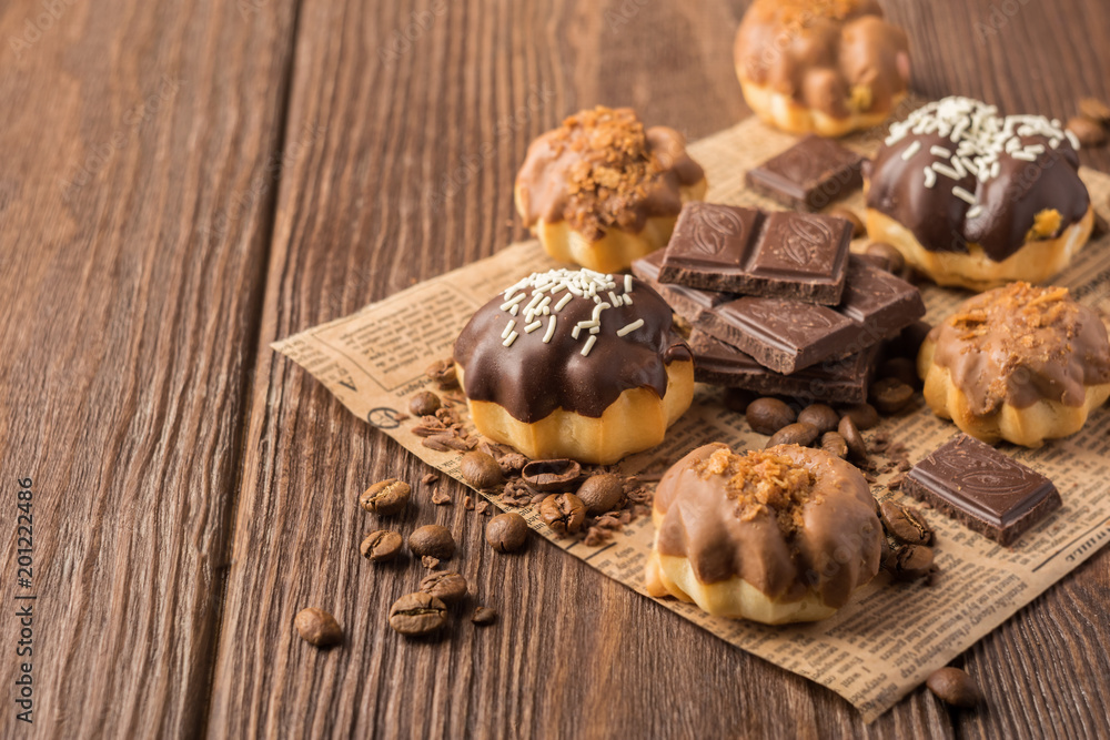 Fresh air dessert chocolate profiterole with a delicate cream decorated with a glaze of milk and dark chocolate on a dark wooden background. Fresh air dessert chocolate profiterole with a delicate cream decorated with a glaze of milk and dark chocolate on a dark wooden background.