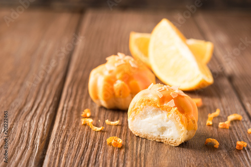 Fresh air cake Profiterrol with a delicate cream decorated with orange glaze on a wooden background.