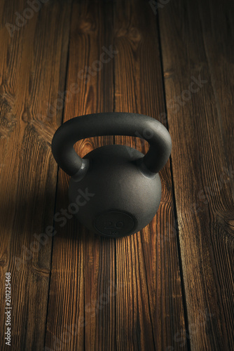 Fototapeta Naklejka Na Ścianę i Meble -  Top view of black iron kettlebell on wooden background Sport equipment background with copyspace Weight lifting exercise concept