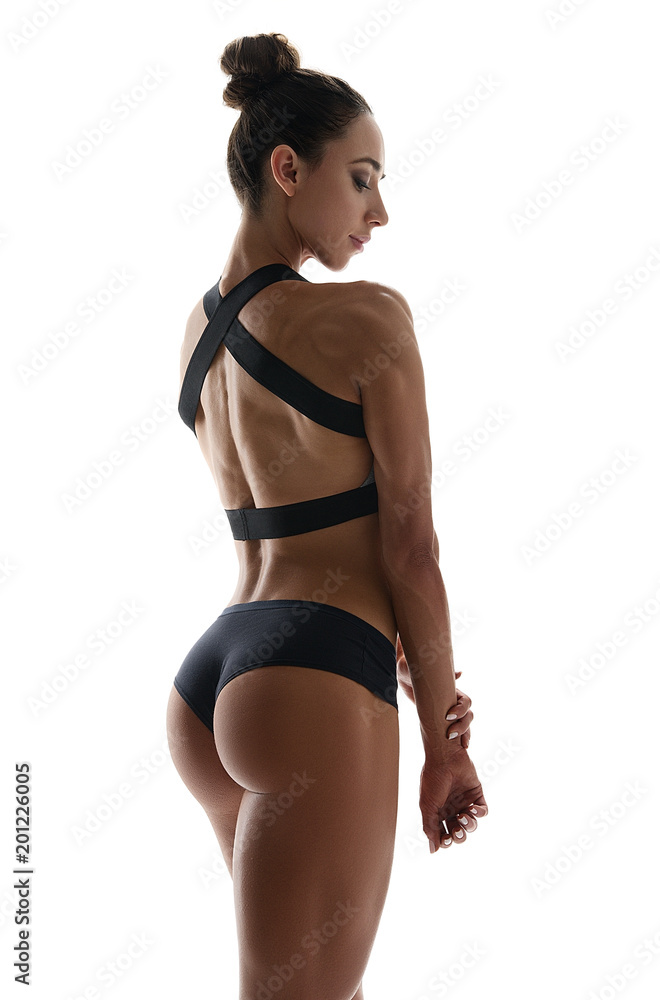 Muscular young woman athlete in sports clothing standing turning back  looking down on white background. Woman bodybuilder relaxing after exercise.  Stock Photo
