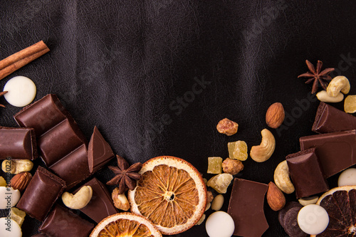 Pieces of chocolate with nuts and circles of dried grapefruit on black leather with a place under the text