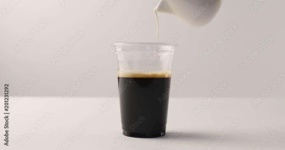 Pouring milk from jug in plastic cup with coffee on white background with reverse footage Pouring milk from jug in plastic cup with coffee on white background with reverse footage