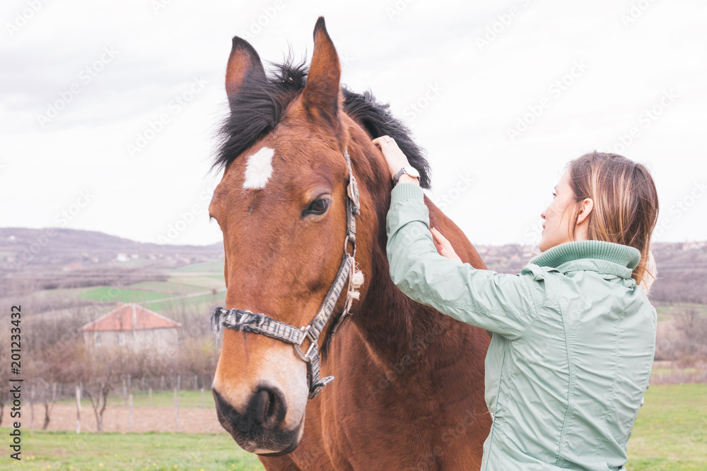 Obraz premium Beautiful young woman on the ranch bonding with a brown horse