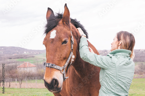 Beautiful young woman on the ranch bonding with a brown horse