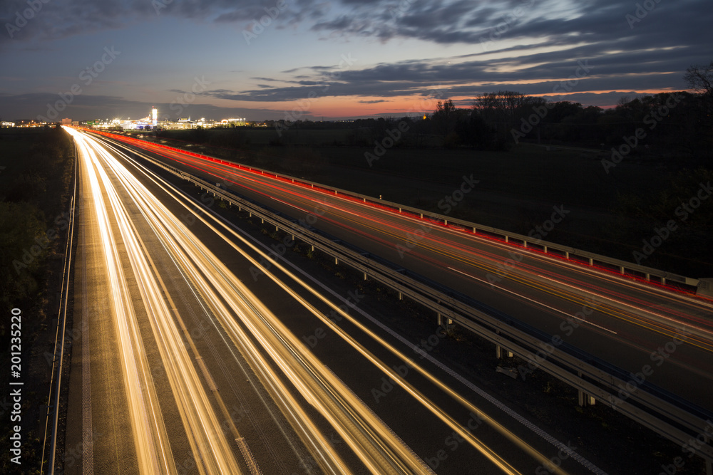 Motion blurred light tracks glowing to the darkness of highway traffic to the city just after sunset. Creative long time exposure photography. Motion blurred light tracks glowing to the darkness of highway traffic to the city just after sunset. Creative long time exposure photography.