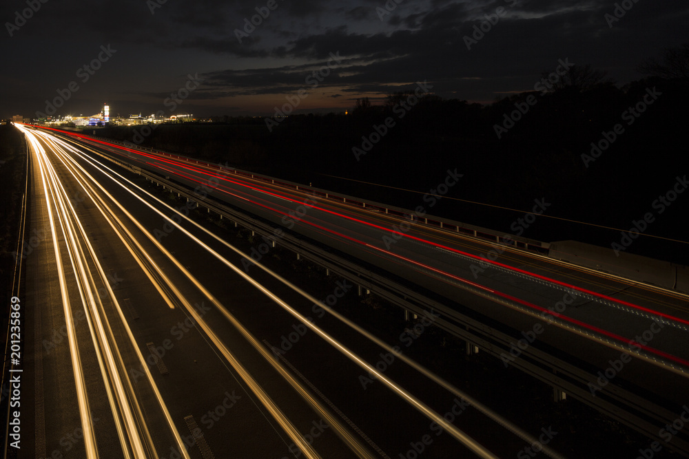Motion blurred light tracks glowing to the darkness of highway traffic to the city just after sunset. Creative long time exposure photography.