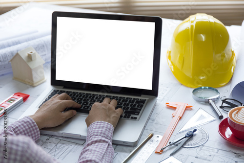 Close-up Architect or engineer hands using tablet working on blueprint plans  with  a pencil,  a ruler, calculator, smartphone, laptop and engineering tools. 