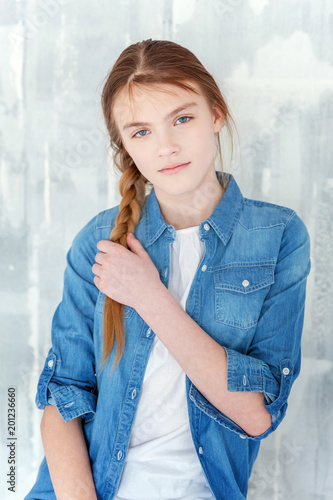 Young Happy Cute Teenage Girl In Jeans Denim Jacket And White T Shirt Sitting On Chair Against Grey Textured Wall Background Casual Daily Lifestyle Schoolgirl Student Education And School Concept Stock Photo