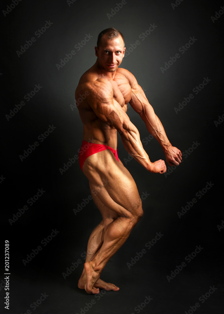 Studio shot of male bodybuilder posing, showing front and side muscles with black background. Studio shot of male bodybuilder posing, showing front and side muscles with black background.