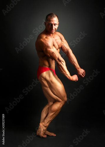 Studio shot of male bodybuilder posing, showing front and side muscles with black background.