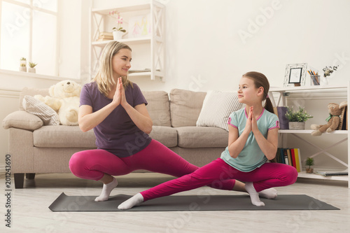 Young woman and child daughter doing yoga exercise at home