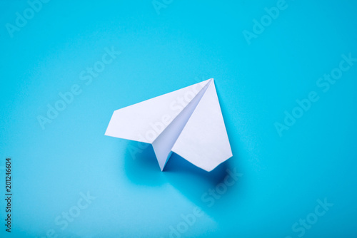 White paper origami airplane lies on pastel blue background