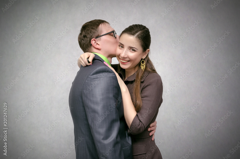 Young business couple is kissing and smiling isolated on gray background. Loving relationships at work concept. Young business couple is kissing and smiling isolated on gray background. Loving relationships at work concept.