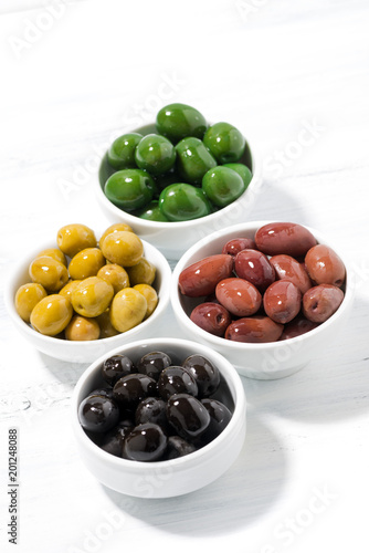 assortment of different kinds of organic olives on white table, vertical