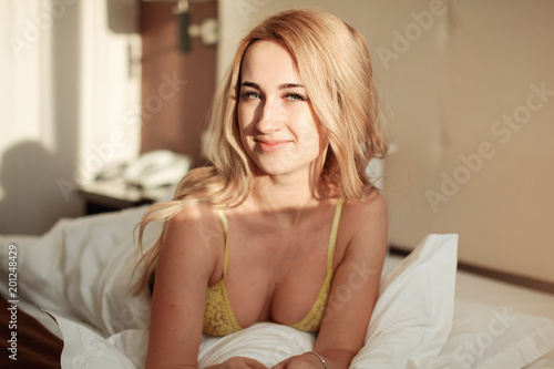 Pretty young woman on bed in modern apartment smiling after wake up