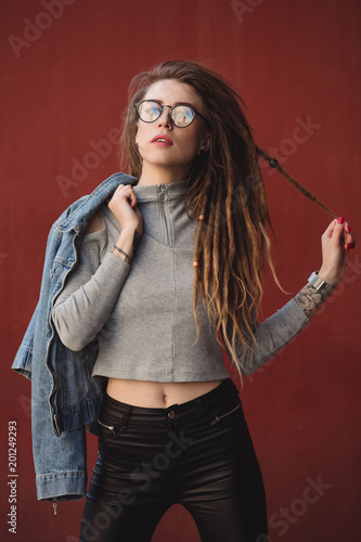 Stylish woman with dreadlocks posing against red wall background