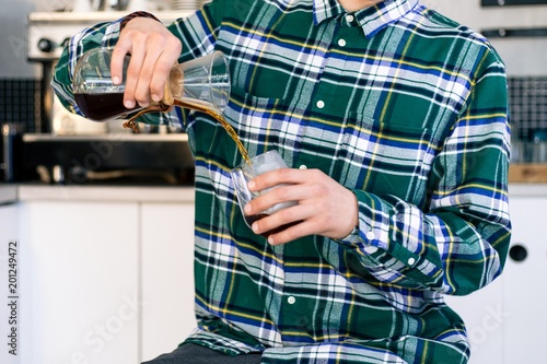 Barista in a green checkered shirt pours a drink into a glass