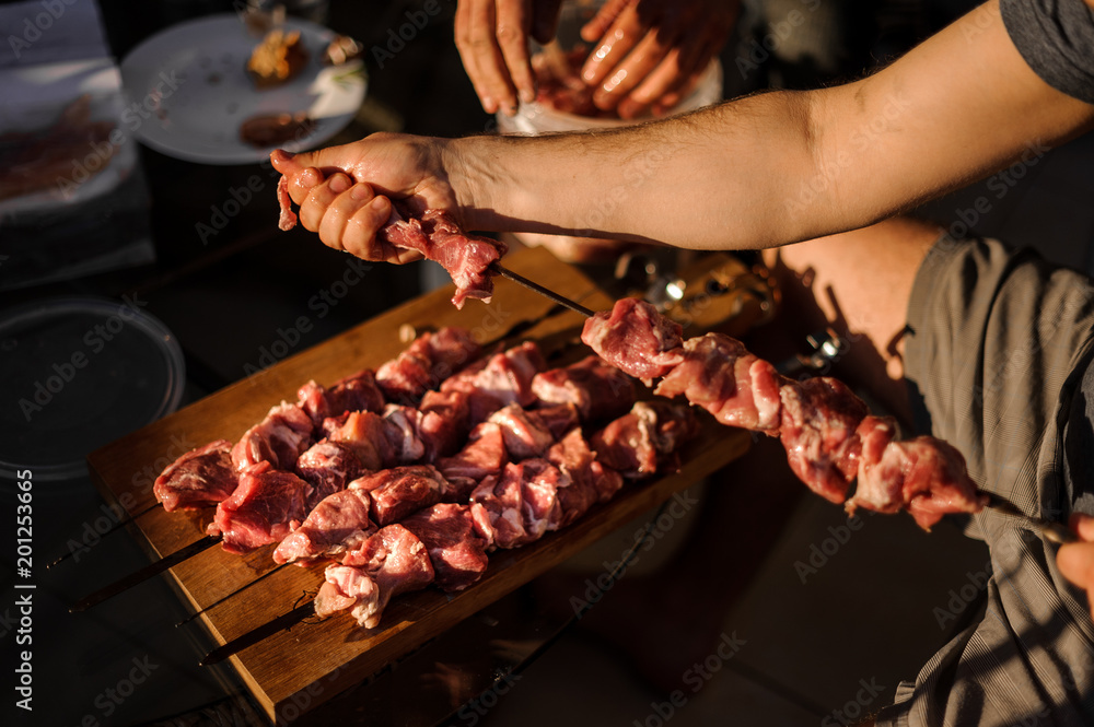 Man string a large meat pieces on the skewer and place them to the cutting board