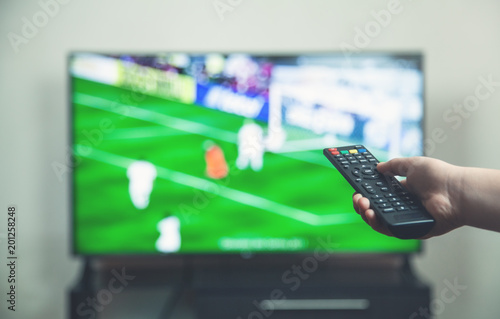  Watching football match on tv with remote controller.