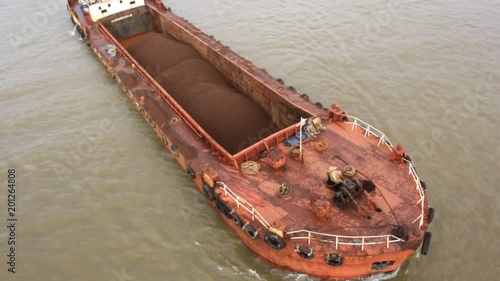 Aerial shot of barge transporting bulk cargo of iron ore mined in hinterland to the main harbor for loading into large ships for exporting, along Zuari River in Goa, India