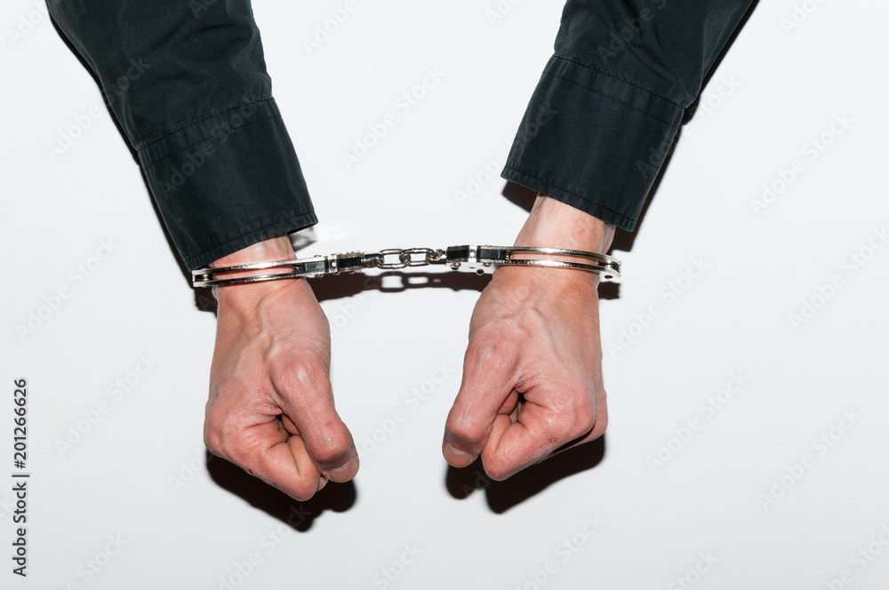Handcuffed hands of arrested criminal man in handcuffs on table in