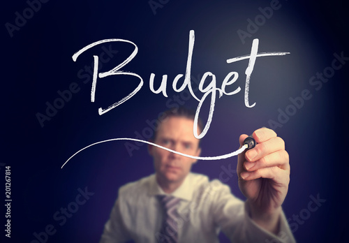 A businessman writing a Budget concept with a white pen on a clear screen.