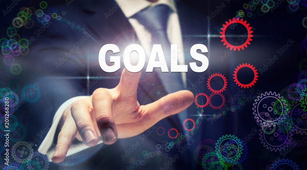 A businessman pressing a Goals business concept on a graphical display of cogs A businessman pressing a Goals business concept on a graphical display of cogs